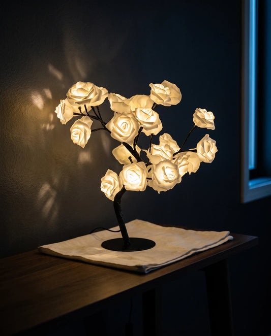 The Lumivano Blossom lit on a dark walnut console table at night, its cream-white roses throwing a dappled warm pattern across the charcoal wall behind, with the cable running down behind the table leg.