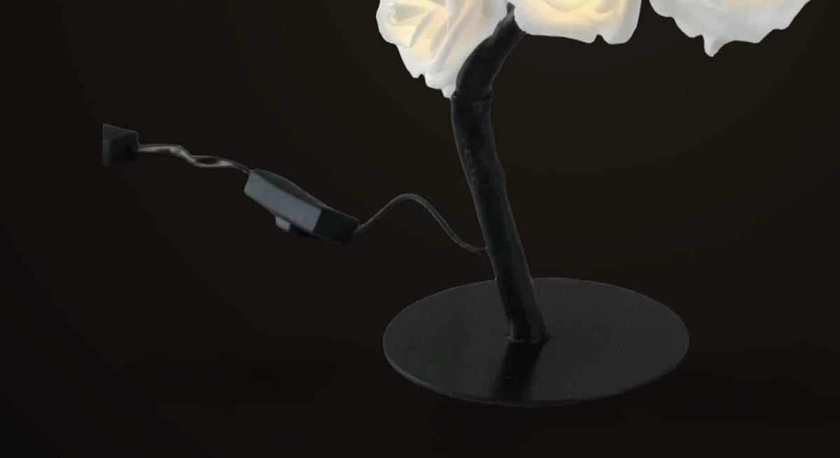 Detail of the Lumivano Blossom on the dark brand ground: the round black base, the black cable coming out of it, the small inline on/off switch on the cable and the USB plug at its end.