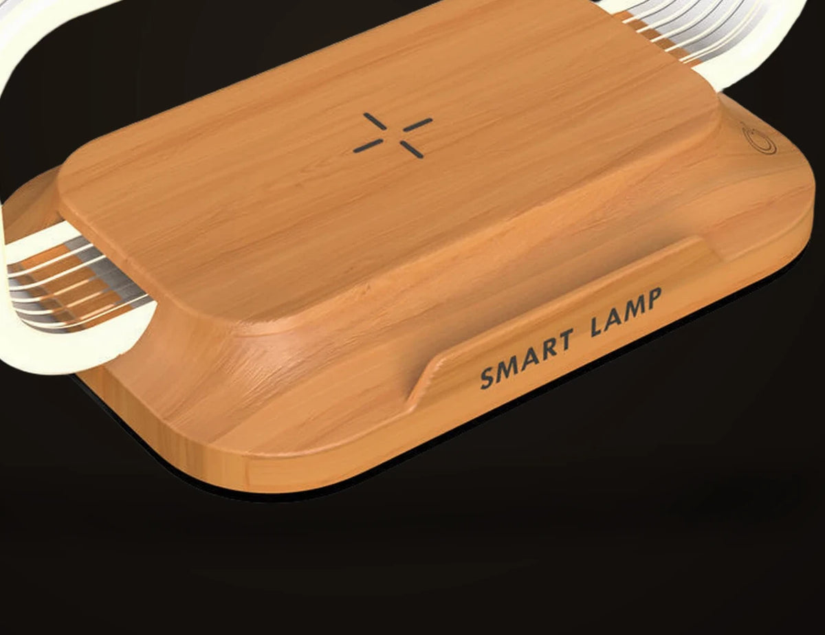 Close view of the base of the Lumivano Lintel on the dark brand ground: the honey-coloured wood-look top panel with its small cross-shaped charging mark, the round touch symbol at the right, the clear acrylic strips of the hoop entering the side of the base, and SMART LAMP printed on the front lip.