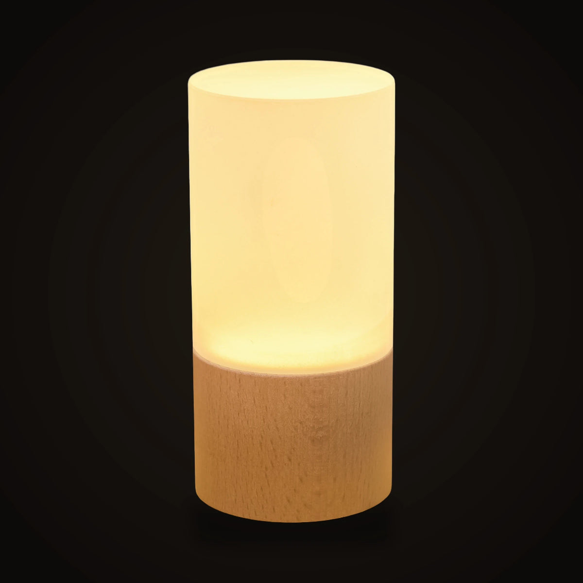 The night light switched on, on the dark brand ground: a plain frosted white acrylic cylinder glowing softly from inside, standing on a round light wooden base of the same width with a fine grain.